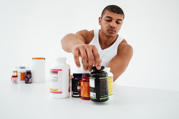 Esportista de pé sobre uma parede branca segurando vitaminas