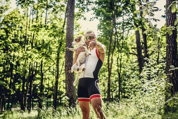 Esportista em roupas esportivas e óculos de sol com seu cachorrinho na floresta verde.