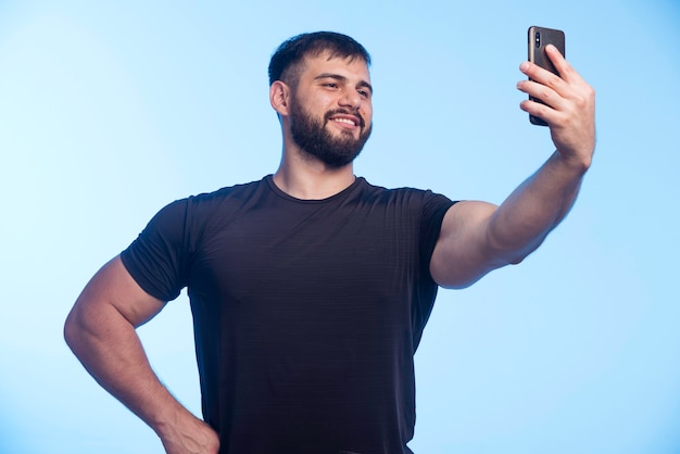 Esportivo homem de camisa preta segura o telefone e tomando selfie.