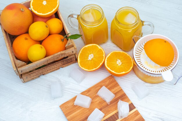 Espremedor de laranja dois copos de suco de laranja uma caixa de madeira cheia de laranja na superfície branca