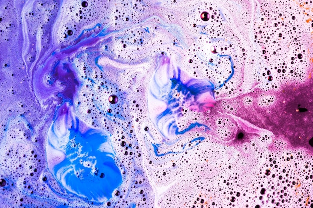 Espuma-de-rosa e azul após bomba de banho cor dissolvendo em água