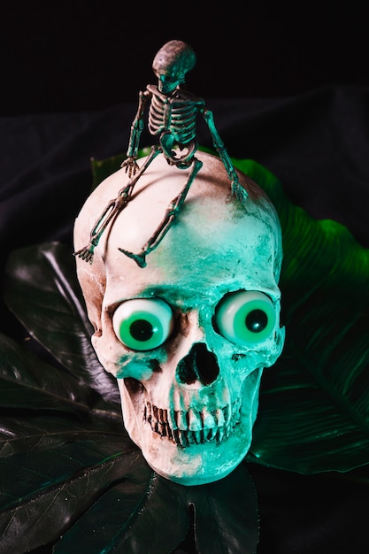 Esqueleto de brinquedo pequeno sentado no crânio assustador