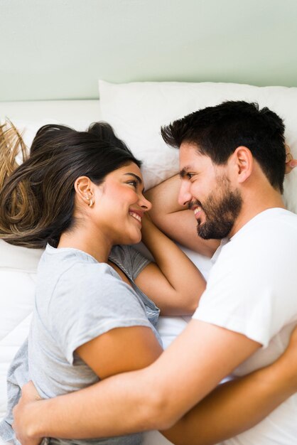 Estamos apaixonados. Casal jovem atraente olhando nos olhos um do outro e sorrindo enquanto abraçando e descansando juntos na cama durante a manhã