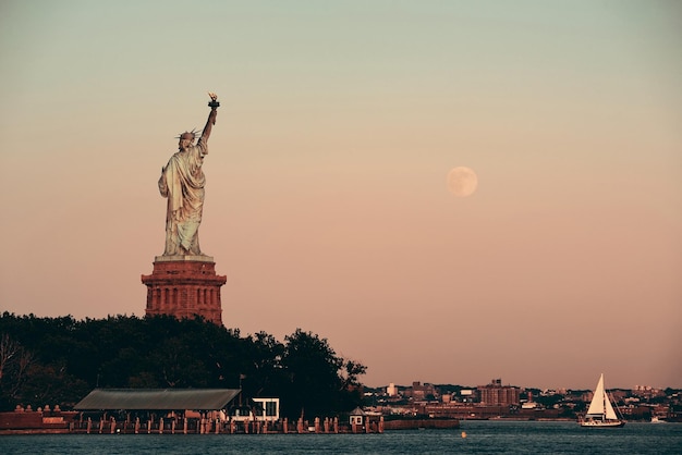 Estátua da Liberdade e lua cheia ao pôr do sol em Nova York