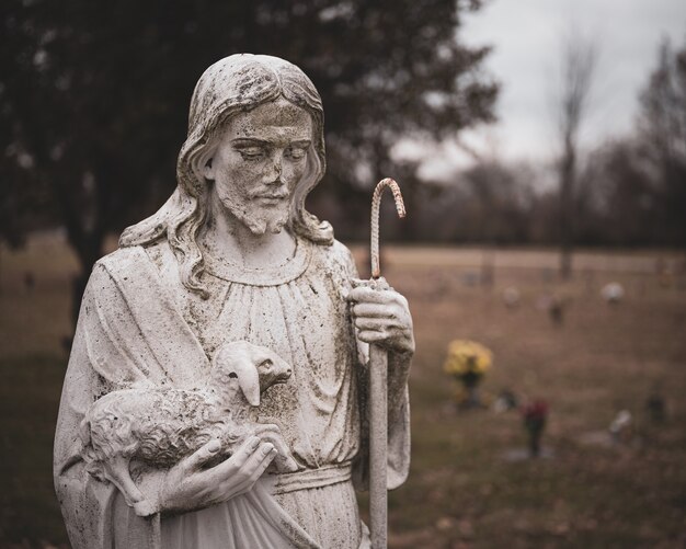 Estátua de Jesus Cristo desgastada com uma ovelha nas mãos em um fundo desfocado