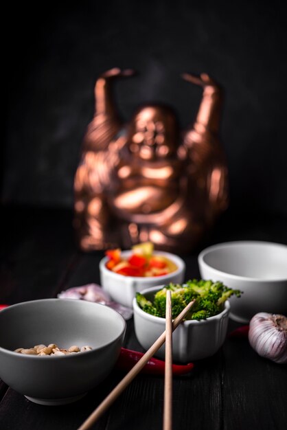 Estátua desfocada com xícaras de legumes e pauzinhos