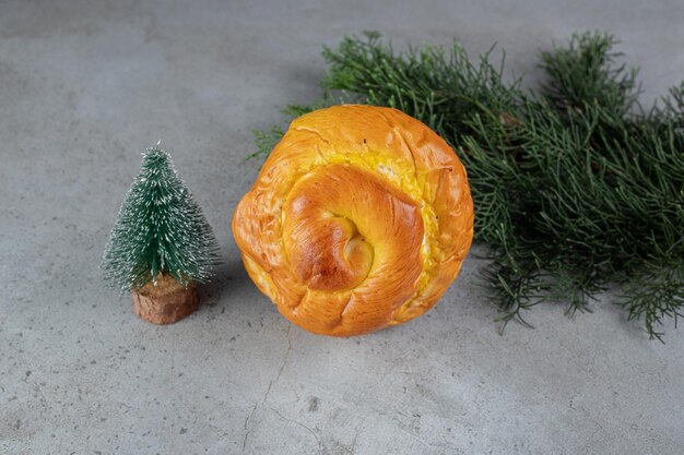 Estatueta de árvore pequena, pão doce e galho de pinheiro dispostos na mesa de mármore.