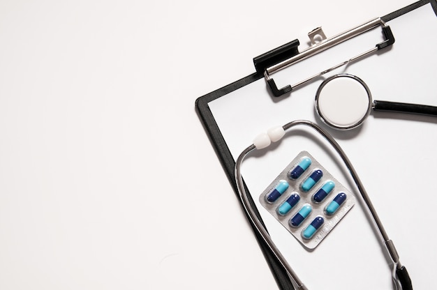 Foto grátis estetoscópio com pílulas de remédio na prancheta médica, conceito médico. conceito de cuidados de saúde.