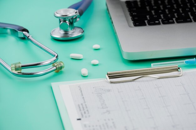 Estetoscópio; pílulas laptop e relatório médico na área de transferência sobre o pano de fundo colorido