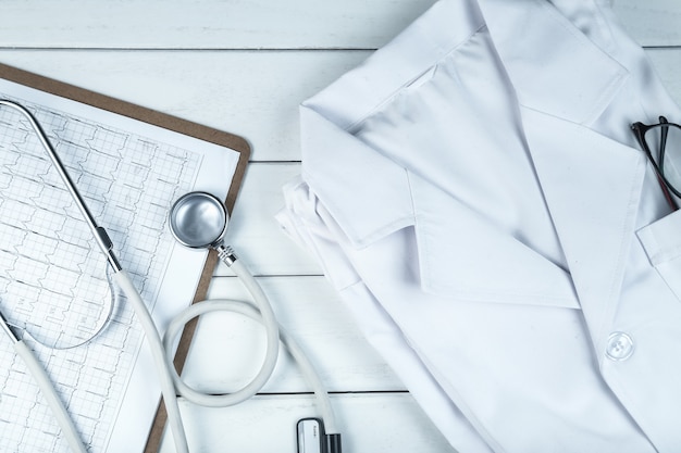 Foto grátis estetoscópio, prancheta e uniforme de médico na mesa de madeira branca e limpa