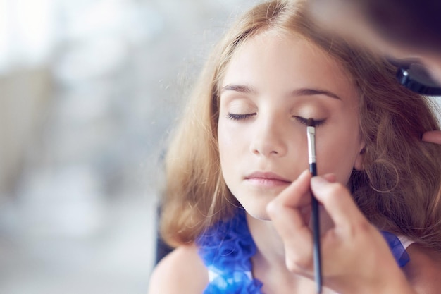 Estilista fazendo a maquiagem para uma linda modelo de menina. Imagem de close-up.