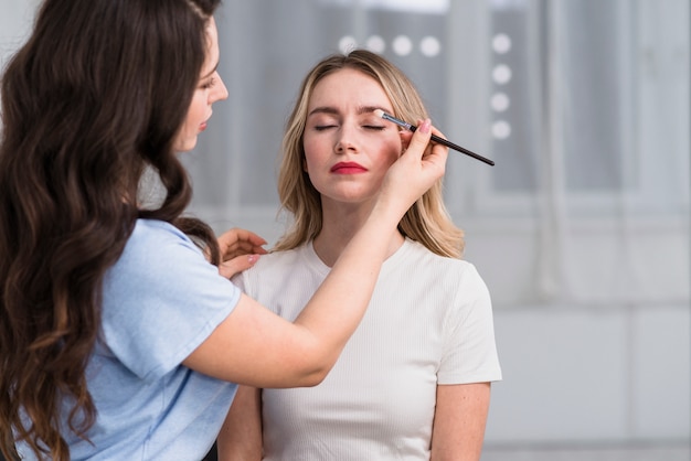 Estilista fazendo maquiagem de sombra para mulher loira