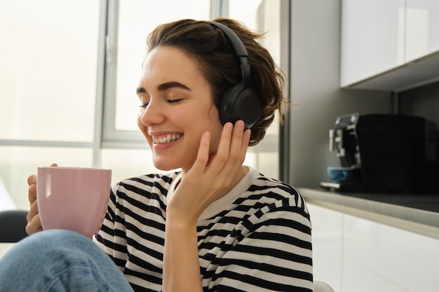 Foto grátis estilo de vida e conceito de música feliz mulher sorridente com uma xícara de chá senta-se na cozinha e toca