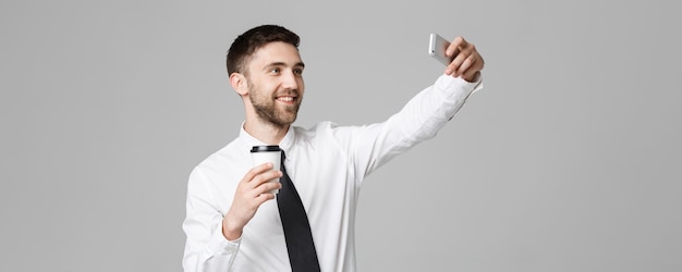 Estilo de vida e conceito de negócios Retrato de um empresário bonito gosta de tirar uma selfie com uma xícara de café para viagem Fundo branco isolado Espaço para cópia