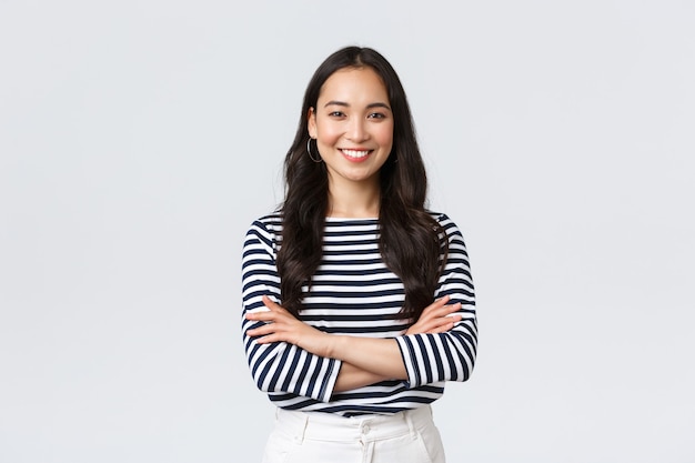 Foto grátis estilo de vida, emoções das pessoas e conceito casual. mulher asiática sorridente confiante e bonita com os braços cruzados, confiante, pronta para ajudar, ouvindo colegas de trabalho, participando da conversa