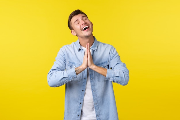 Estilo de vida, emoções das pessoas e conceito de lazer de verão. esperançoso encantado e aliviado bonito homem sorridente se sentindo feliz, de mãos dadas em orar feche os olhos e agradecendo a deus, sendo grato.