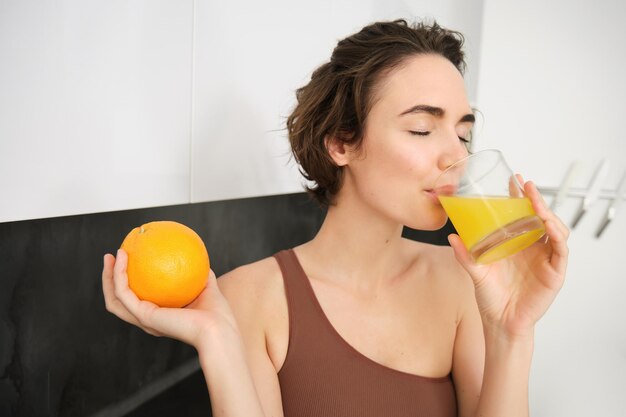 Estilo de vida saudável e esporte linda mulher sorridente bebendo suco de laranja fresco e segurando frutas