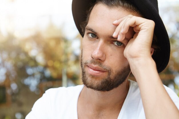 Estilo e moda. Foto altamente detalhada do jovem modelo caucasiano com barba hipster usando chapéu preto na moda