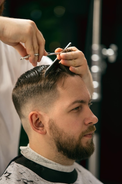 Estilo fresco. Feche o cliente do mestre barbeiro, estilista durante o atendimento e novo visual do penteado. Ocupação profissional, beleza masculina e conceito de autocuidado. Cores suaves e foco, vintage.