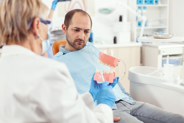 Estomatologista explicando a higiene dental adequada usando o esqueleto dos dentes durante a consulta de estomatologia