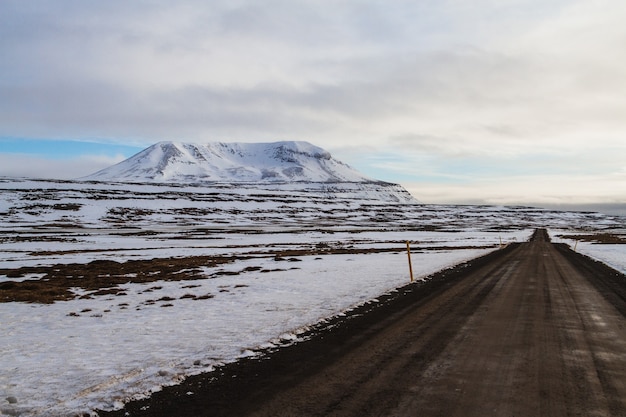 Estrada cercada pelo campo e pelas rochas cobertas de neve sob um céu nublado na Islândia