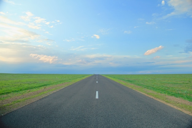 Foto grátis estrada cercada por campos de grama sob um céu azul