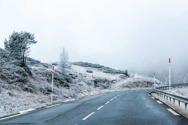 Estrada cercada por montanhas nevadas cobertas pela névoa