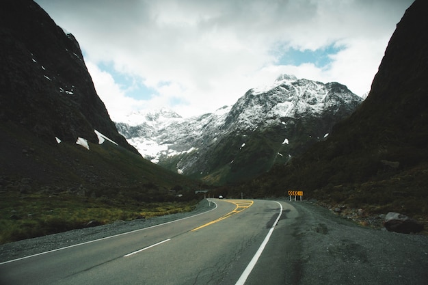 Foto grátis estrada curvilínea no campo com montanhas nevadas e belas nuvens no céu