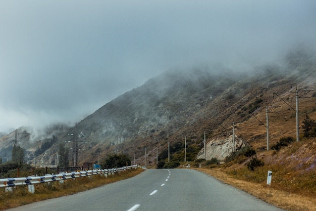 Estrada perto de altas montanhas envolvidas no nevoeiro