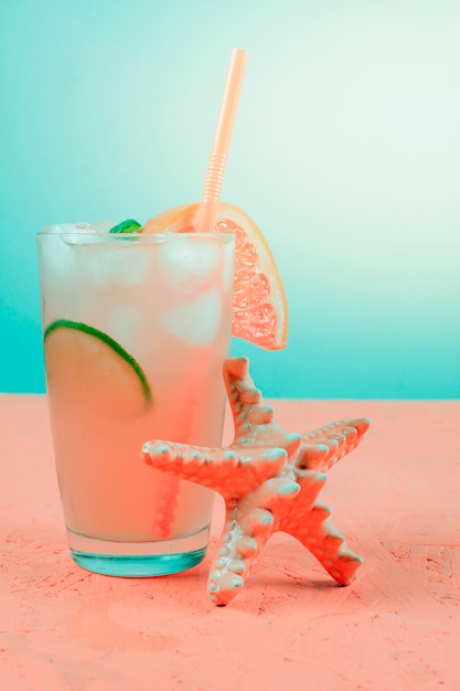 Estrela do mar perto do cocktail de toranja na mesa de coral contra o fundo azul-petróleo