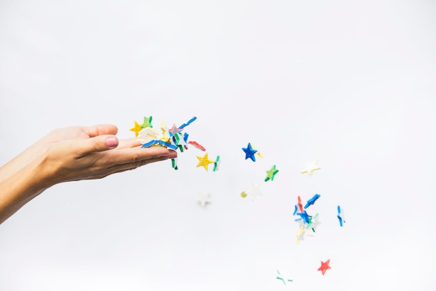 Estrelas coloridas soprando das mãos femininas isoladas contra o pano de fundo branco