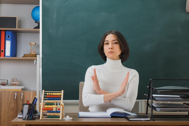 estrito não mostrando nenhum gesto jovem professora sentada na mesa com ferramentas escolares na sala de aula