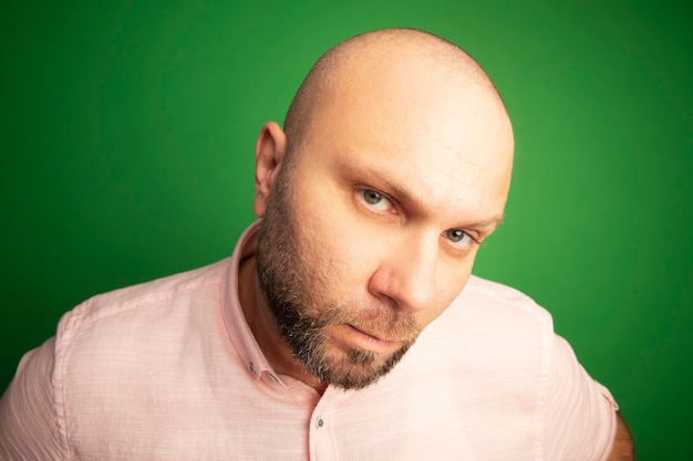 Foto grátis estrito olhando para a frente, homem careca de meia-idade vestindo camiseta rosa isolada no verde