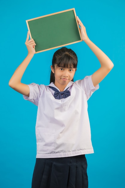 Foto grátis estudante asiática com menina de cabelos longos, segurando uma placa verde em um azul.