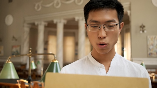 Estudante asiático excitantemente abrindo envelope com resultados de exames na biblioteca da universidade