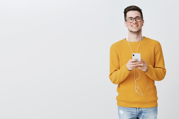 Estudante bonita de óculos ouvindo música com fones de ouvido e mensagens via smartphone