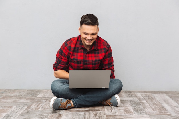 Estudante de homem trabalhando no laptop enquanto está sentado no chão