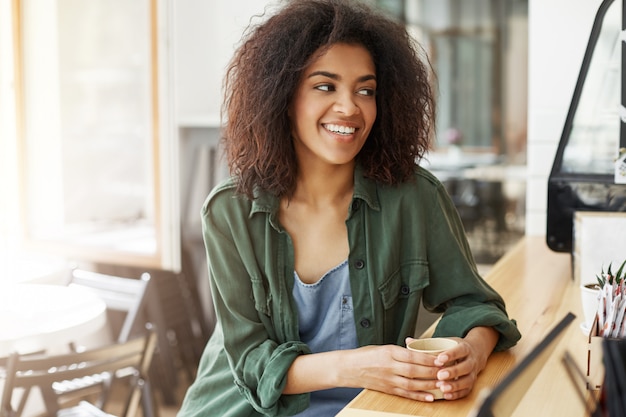 Estudante de mulher africana bonita jovem descansando relaxante sentado no café sorrindo bebendo café.