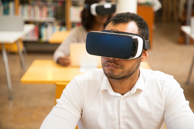 Estudante do sexo masculino adulto usando óculos VR enquanto trabalhava na biblioteca