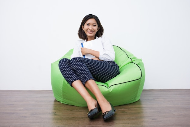 Foto grátis estudante fêmea asiático feliz que descansa em beanbag