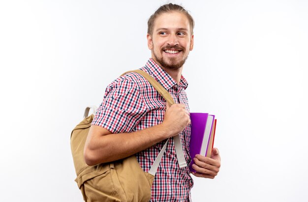 Estudante jovem sorridente olhando de lado usando uma mochila segurando livros