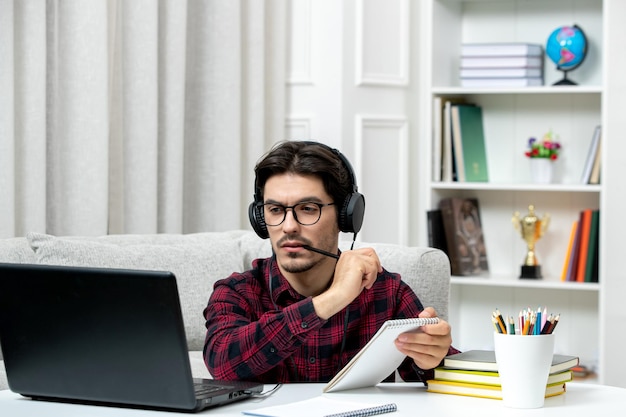 Estudante on-line bonitinho de camisa xadrez com óculos estudando no computador pensando concentrado