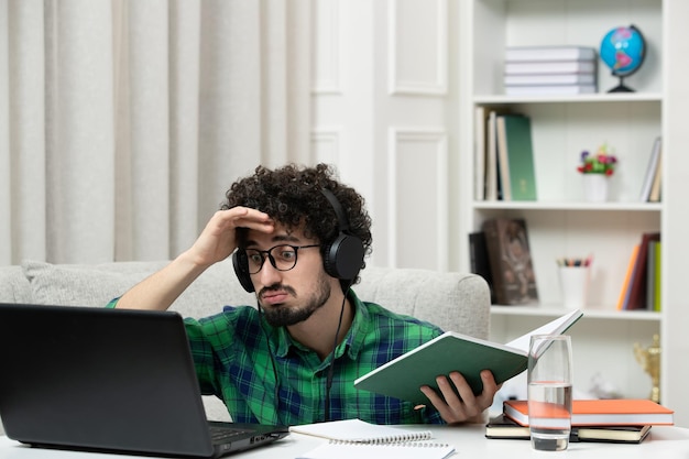 Estudante on-line bonito jovem estudando no computador em óculos de camisa verde confuso segurando a cabeça