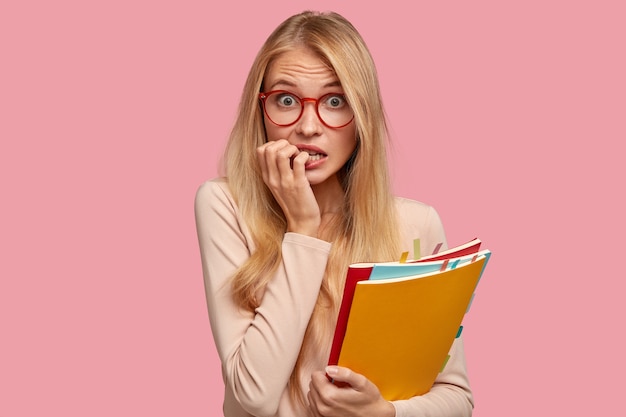 estudante universitária loira ansiosa posando contra a parede rosa