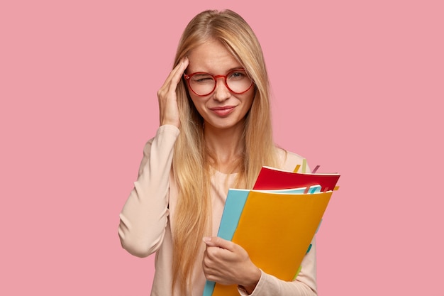 Estudante universitária triste e esquecida posando contra a parede rosa