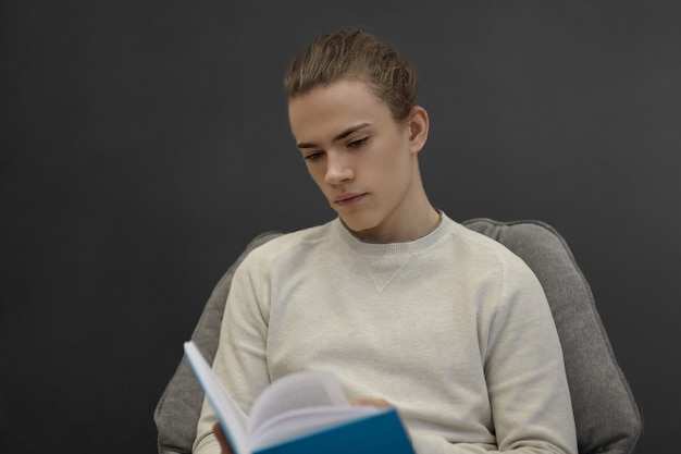 Estudante universitário concentrado, absorto na leitura de algum romance de aventura, sentado na biblioteca da universidade