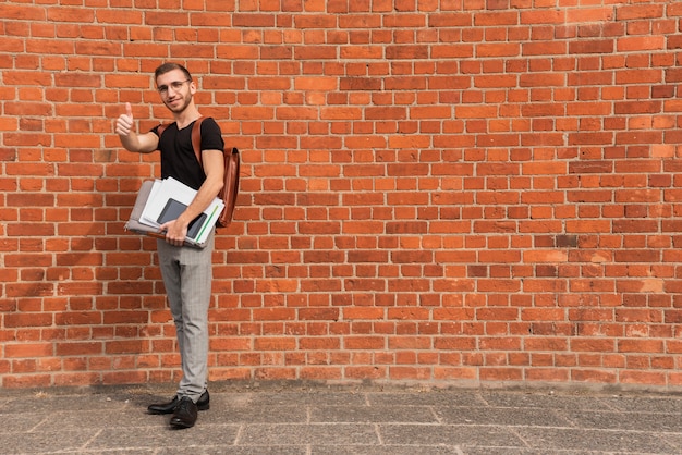 Estudante universitário em pé na frente de um fundo de espaço de cópia de parede de tijolo