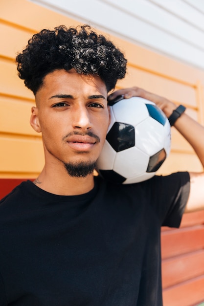 Étnico homem com bola de futebol no ombro