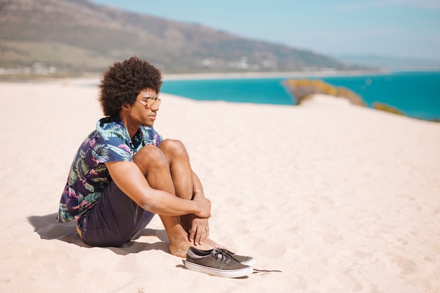 Étnico masculino sentado com os pés descalços na praia