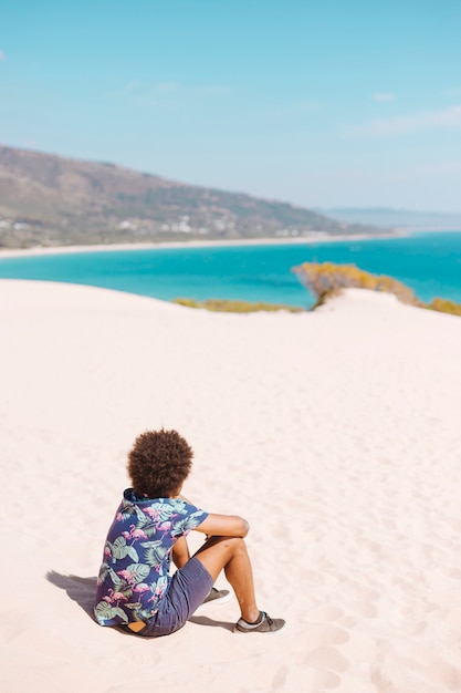 Étnico masculino sentado na areia da praia